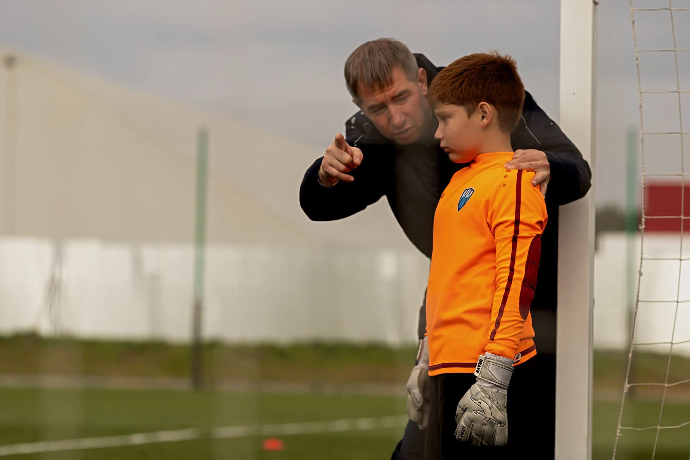 A coach providing guidance to a young goalkeeper on a soccer field.